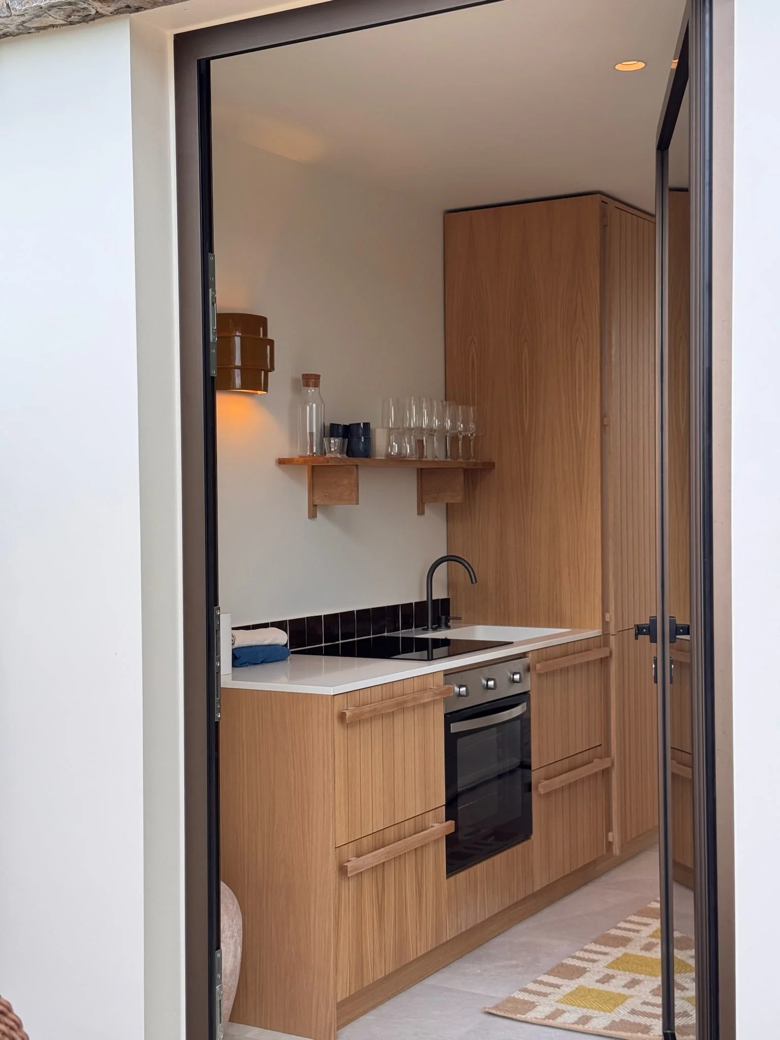 Kitchenette in light wood behind a steel-framed glass door — Anse des Cayes