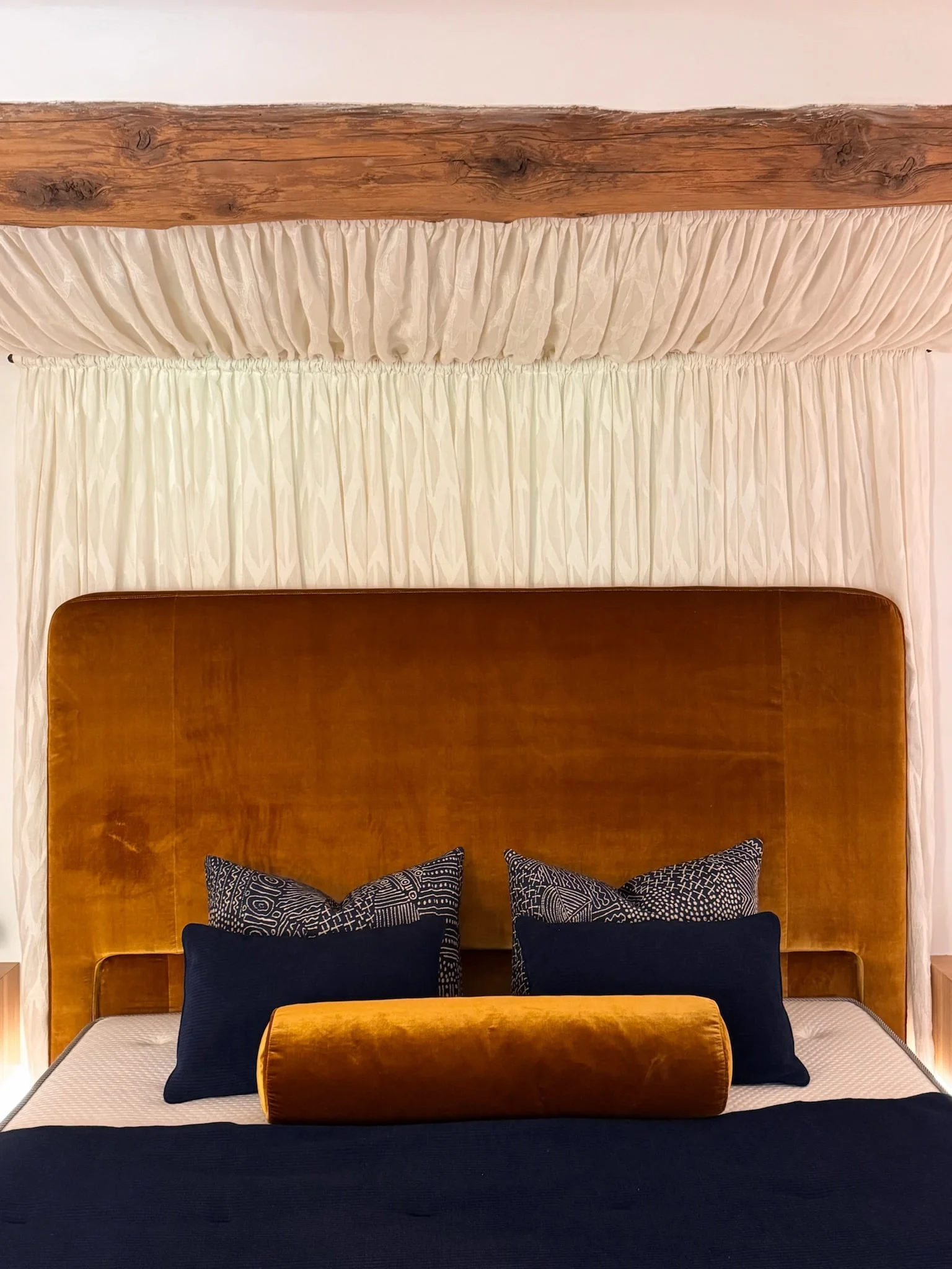 Bed with ochre velvet headboard beneath a gathered fabric canopy — Fontaine