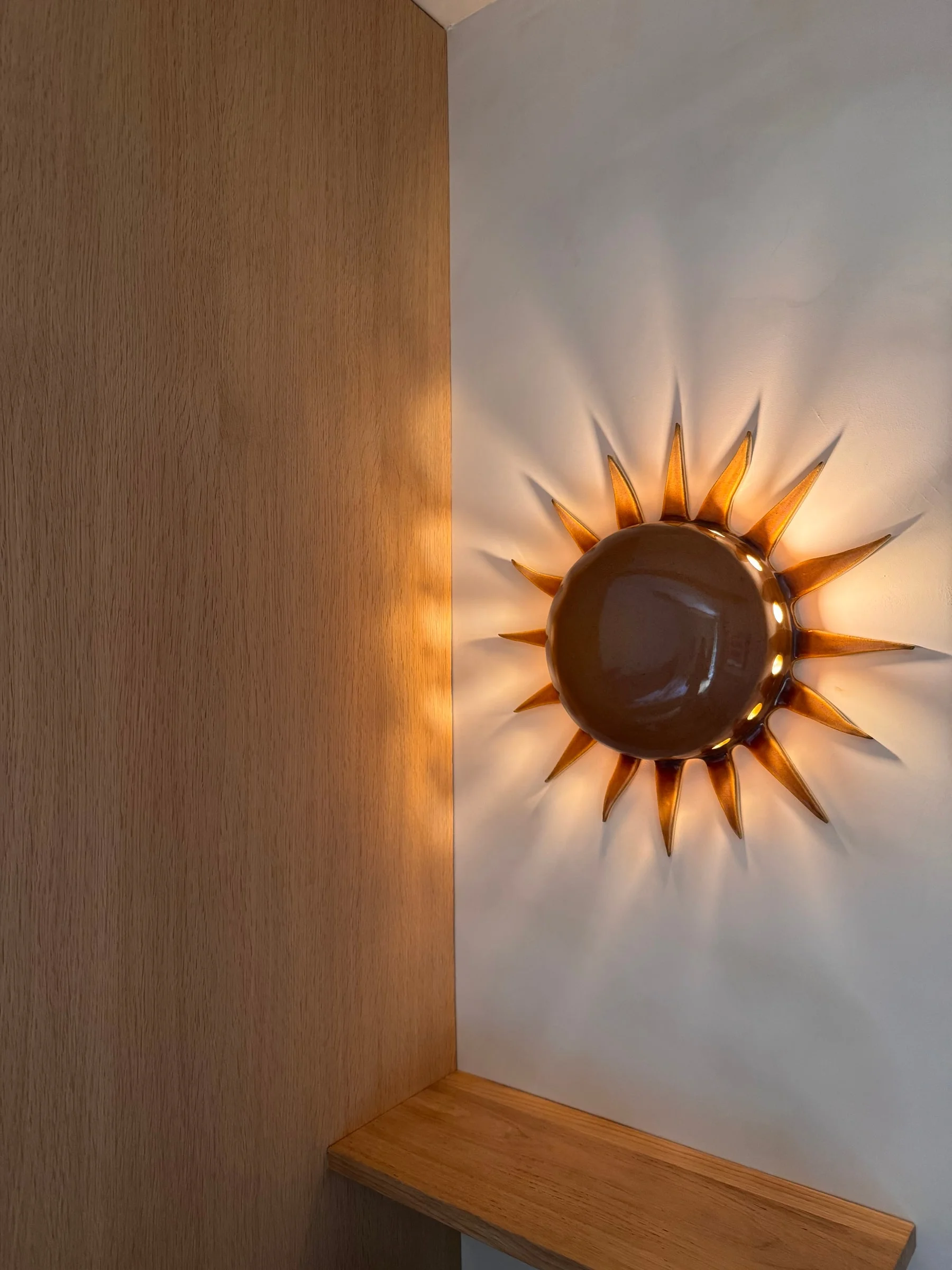Sunburst wall light above an oak shelf — Fontaine