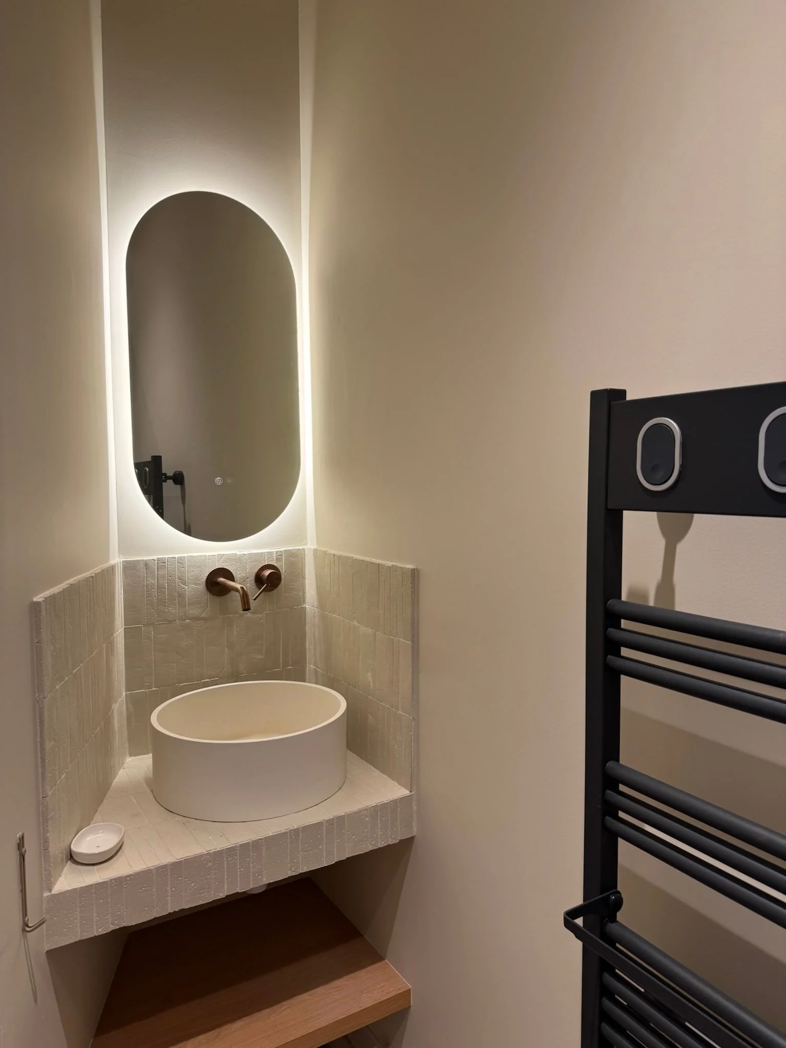 Round washbasin beneath a backlit oval mirror — Petite Fontaine